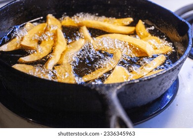 Hand cut french fried potatoes frying in a cast iron skillet.
