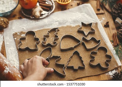 Hand cutting raw dough with  metal cutters and anise, ginger, cinnamon, pine cones, fir branches on rustic table. Making christmas gingerbread cookies. - Powered by Shutterstock