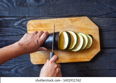 Hand cutting vegetables in kitchen. Female slicing a big eggplant on cutting board.