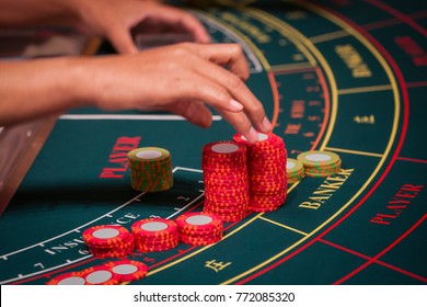 A Hand of Dealer Organizing the Red and Green Baccarat Chips on Baccarat Gaming table.