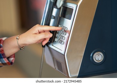 A hand dials a number on an old payphone