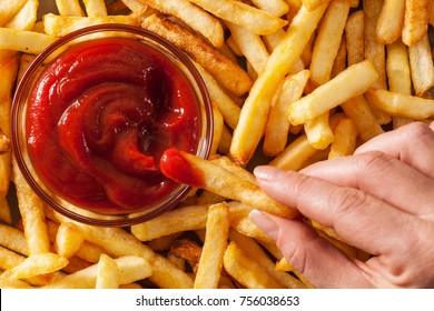 Hand dipping french fries in tomato sauce or ketchup - top view, closeup