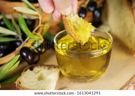 A hand dipping a piece of bread in a bowl full of Extra Virgin Olive Oil made in Puglia, Salento on a wooden table. Tipical ingredients of mediterranean diet, healhty eating concept