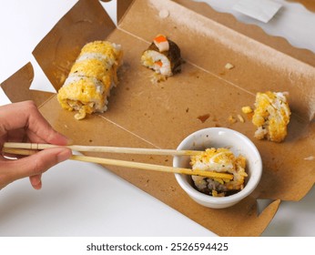 A hand dipping a sushi roll into soy sauce using chopsticks, in a partially eaten sushi takeout box. A delicious moment of enjoying fresh sushi. - Powered by Shutterstock