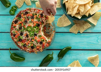 A Hand Dipping A Tortilla Chip Into A Homemade Mexican 7 Layer Dip.