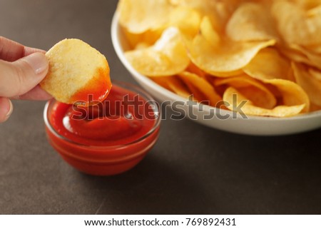 Hand dips crispy chip into tomato sauce in glass bowl. Concept unhealthy party food for friday.
