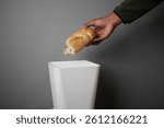 Hand discarding bread into a trash bin in a minimalistic setting
