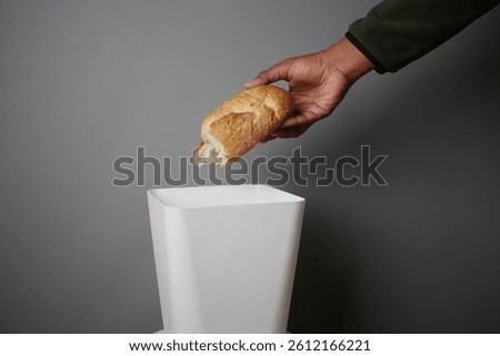 Hand discarding bread into a trash bin in a minimalistic setting
