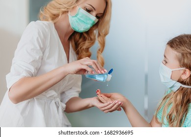 Hand disinfection during coronavirus - mother holding sanitizer and sanitizing hands of a little girl wearing face mask - Powered by Shutterstock