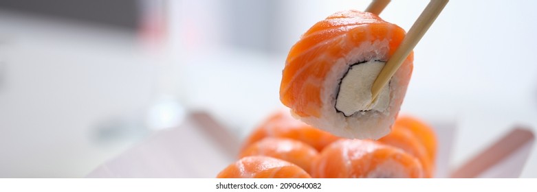 Hand with disposable chopsticks holds sake nigiri sushi with salmon fish