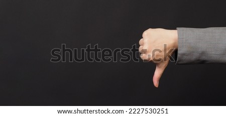The hand do dislike or thumbs down hand sign on black background. Hand wear grey suit.