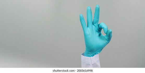Hand is do A OK hand sign and wear doctor gown and blue medical glove on grey background. Studio shooting.