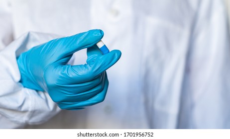 The hand of a doctor or pharmacist in blue gloves holds a capsule with medicine - Shutterstock ID 1701956752