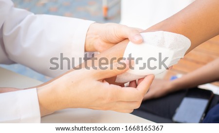 hand of Doctor is using clean cotton dressing infection wound at a women arm. Bandage for wound dressing at a clinic. medical care healthcare insurance concept.