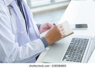 Hand Of Doctor Writing Note On Notebook With Laptop Computer On Background.