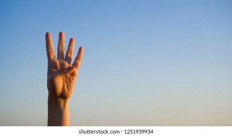 Hand doing / showing number four gesture symbol on blue summer sky nature background. Gesturing number 4. Number four in sign language. Fourth, counting down four concept. Four fingers up. Rabia sign