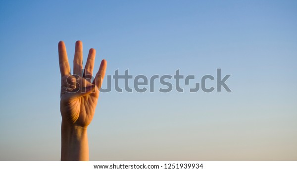 Hand doing / showing number four gesture\
symbol on blue summer sky nature background. Gesturing number 4.\
Number four in sign language. Fourth, counting down four concept.\
Four fingers up. Rabia\
sign