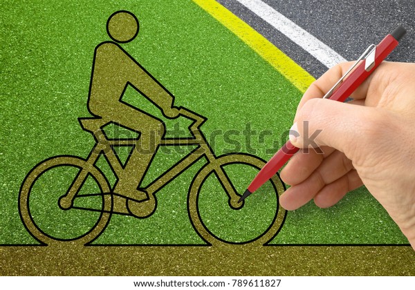 Hand drawing a bicycle silhouette on a\
green asphalt bicycle lane - concept\
image