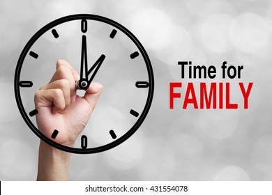Hand is drawing a clock with text Time For Family Concept aside with blurred gray background.