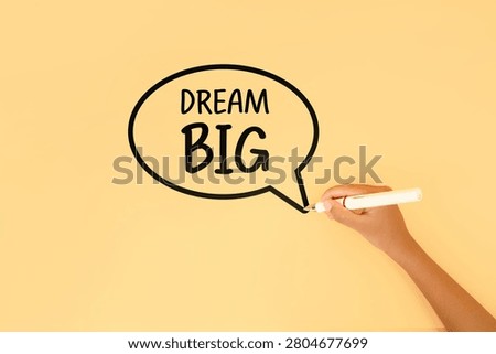 Hand drawing a dream big message inside a speech bubble on a pastel background. Concept of ambition, motivation, goal setting, personal growth and success mindset.