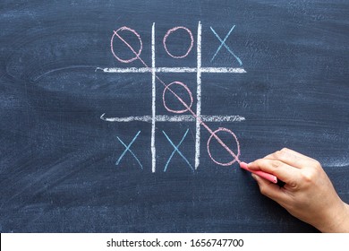 hand drawing a game of tic tac toe with colored crayons on a black chalkboard
