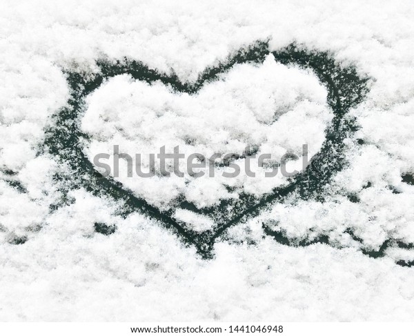 Hand drawn heart shape on the snow of car\
windshield. Love symbol design close\
up
