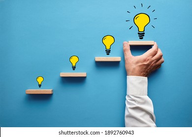 Hand drawn light bulbs representing a developing new idea on wooden steps with male hand placing the last step. Idea development, business vision or entrepreneurship concept.