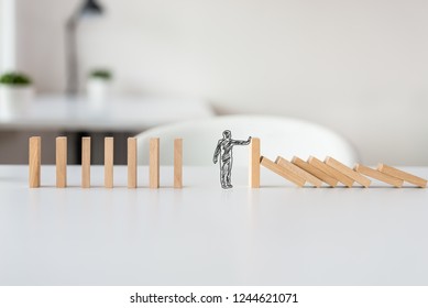 Hand drawn shape of businessman stopping domino effect in a conceptual image of solving business crisis.