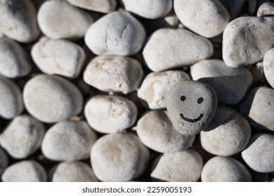 hand drawn smile on a small gray stone. The smiling stone lies on top of other stones in the background - Shutterstock ID 2259005193