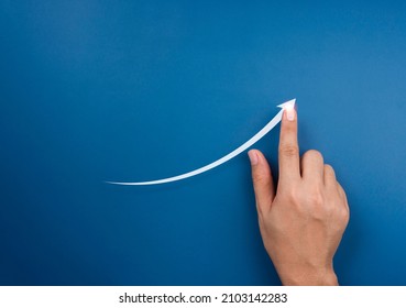 Hand draws a rising arrow on blue background. Finger pointing on the shining arrowhead, minimal style. Business growth and success concept. Increase business opportunities.