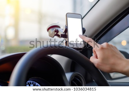 Hand of driver using smartphone which holding on magnet phone mount holder at the car windshield with screen for map GPS navigation on the traffic road background