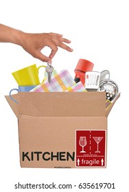 Hand Dropping Keys Into Open Moving Box Filled With Cups, Flashlight, Paper Plates, Kitchen Utensils Isolated On White Background