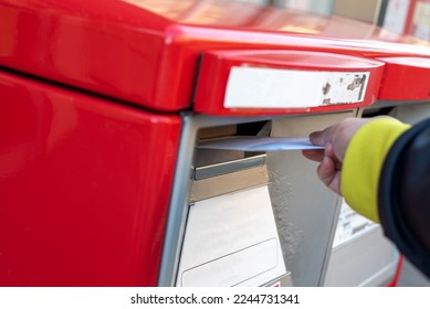 A hand dropping off an envelope into a red post mail box 