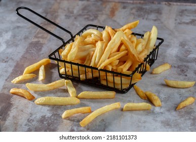 Hand Dropping Some Salt On A Black Metal Basket Full Of French Fries On A Gray Surface And Gray Background