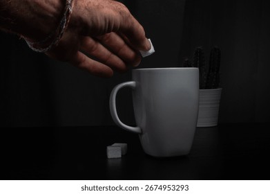 Hand dropping sugar cube into white mug with cactus plant