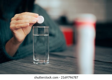 

Hand Dropping A Vitamin Pill Into A Glass Of Water. Person Taking A Natural Supplement Capsule Remedy
