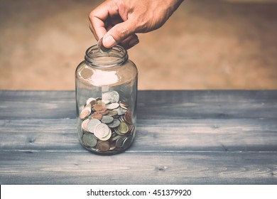 Hand Drops Money Into A Glass Jar For A Savings 