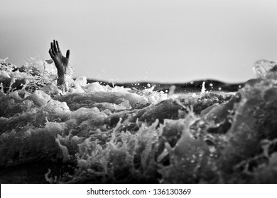 Hand of drowning man trying to swim out of the stormy ocean. Black and white photo.