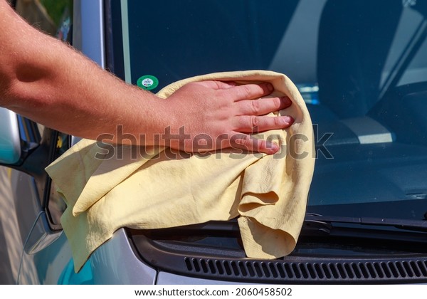 A hand with a\
dry rag wipes the windshield of a car at a car wash. Background\
with copy space for text or lettering. Illustrative editorial. July\
23, 2021, Balti Moldova.