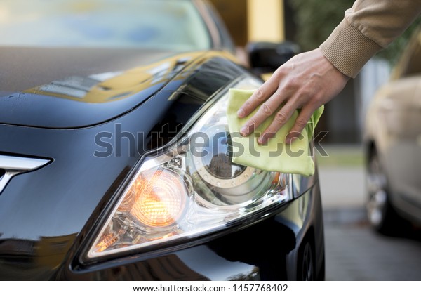Hand with\
duster cleaning headlight of dark\
auto