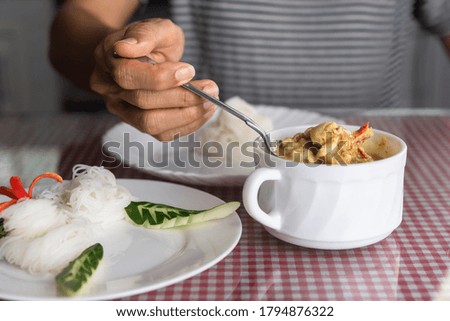 Hand eating Thai green curry and noodle in restaurant