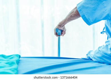 Hand Of Elderly Man With Metal Walking Stick While Sitting On Bed Patient In Hospital. Medical And Healthcare Caretaker Helping Senior Concept. Copy Space