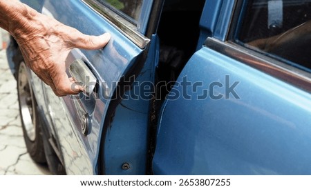Hand of elderly people pull or grab the outside handle to open the car door. Old man attempt to open door of an old blue vintage car. Ageing society, Once upon a time, Nostalgic memories concept.