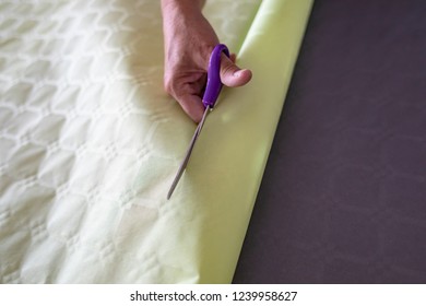 Hand Of An Elderly Woman Cutting Through Green Gift Wrapping Paper With A Pair Of Purple Scissors In Preparation Of Festivities. 