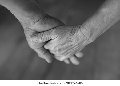 Hand Of An Elderly Woman Holding The Hand Of An Elderly Man. Black And White.