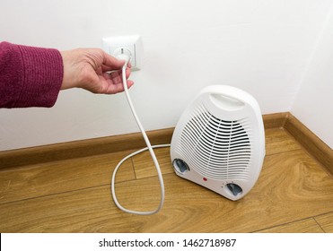 The Hand Of An Elderly Woman Plug In Electric Heater In The Socket. Selective Focus, Close-up.