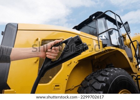 Hand with electric vehicles charging plug on a background of electric tractor
