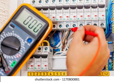 Hand of an electrician with multimeter probe at an electrical switchgear cabinet