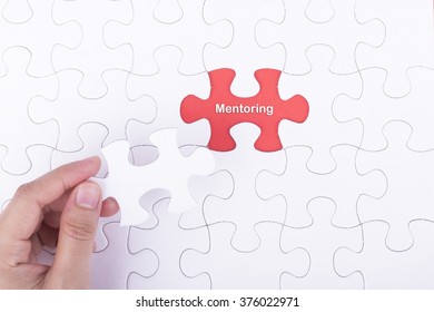 Hand embed missing a piece of puzzle into place, red space with word MENTORING concept.