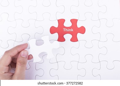 Hand embed missing a piece of puzzle into place, red space with word THINK concept